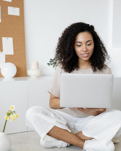 Young woman with curly hair working on her laptop in a cozy home setting, exuding confidence and focus.